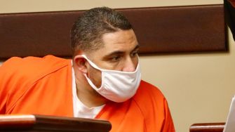 Suspect in custody for freeway shootings, wearing an orange jumpsuit and mask in court.