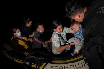 Migrants arriving by boat, including a woman holding a child, as they seek refuge.