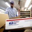 A postal worker handling packages inside a USPS facility, with a focus on a "Priority Mail" box in the foreground. A postal worker handling packages inside a USPS facility, with a focus on a "Priority Mail" box in the foreground.