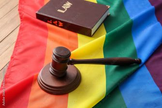 A gavel and a law book resting on a rainbow flag, symbolizing LGBTQ+ rights and legal issues.