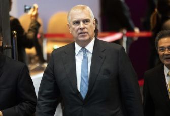 Prince Andrew walking in a formal setting, accompanied by others.