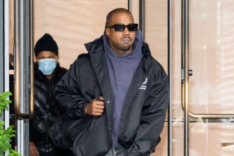 Kanye West, also known as Ye, leaving a building while wearing sunglasses and a mask.