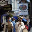 Two women wearing masks walk along a busy street with various shops and signage in the background. Two women wearing masks walk along a busy street with various shops and signage in the background.