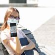 A young woman wearing a face mask holds a smartphone displaying a QR code while seated outdoors. A young woman wearing a face mask holds a smartphone displaying a QR code while seated outdoors.