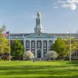 A view of the Harvard University campus featuring the iconic building with a flag and surrounding greenery. A view of the Harvard University campus featuring the iconic building with a flag and surrounding greenery.