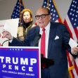 Rudy Giuliani speaking at a press conference with a "Trump Pence" backdrop, discussing election-related claims, while two women stand behind him. Rudy Giuliani speaking at a press conference with a "Trump Pence" backdrop, discussing election-related claims, while two women stand behind him.