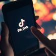 Close-up of a person using a smartphone displaying the TikTok logo on a blurred colorful background. Close-up of a person using a smartphone displaying the TikTok logo on a blurred colorful background.