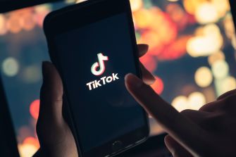 Close-up of a person using a smartphone displaying the TikTok logo on a blurred colorful background.