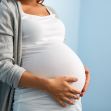 A pregnant woman in a white dress is standing with her hands on her belly against a blue wall. A pregnant woman in a white dress is standing with her hands on her belly against a blue wall.