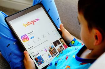 A child holding a tablet displaying the Instagram app interface while seated on a couch.