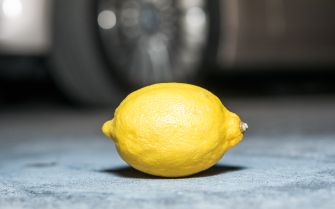 A yellow lemon on a surface, with a blurred background of a vehicle wheel.