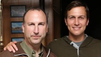 Two men standing close together, one wearing a jacket and the other dressed in a hoodie.