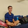 A young male student sitting cross-legged on a bed in a dorm room, smiling at the camera. A young male student sitting cross-legged on a bed in a dorm room, smiling at the camera.