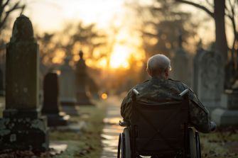 An elderly veteran in a wheelchair sitting in a cemetery during sunset.