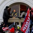 A group of individuals, some holding flags, breach the Capitol building during the January 6 riot, while others look on from inside. A group of individuals, some holding flags, breach the Capitol building during the January 6 riot, while others look on from inside.