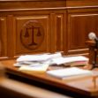 A courtroom interior with a wooden bench, scattered papers, and a microphone, featuring a symbol of justice. A courtroom interior with a wooden bench, scattered papers, and a microphone, featuring a symbol of justice.
