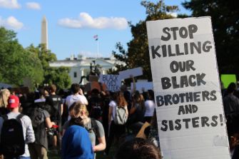 A protest scene highlighting a sign that reads "STOP KILLING OUR BLACK BROTHERS AND SISTERS!" with the Washington Monument in the background.
