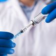 A person in a lab coat holding a vaccination vial and syringe, wearing blue gloves. A person in a lab coat holding a vaccination vial and syringe, wearing blue gloves.