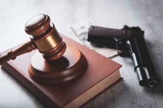 A gavel resting on a law book next to a handgun and cash, symbolizing legal and financial aspects of gun ownership.