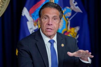 New York Governor Andrew Cuomo speaking at a press conference with state flags in the background.