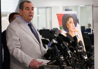 A lawyer speaking at a press conference with a photo of cinematographer Halyna Hutchins in the background.