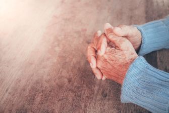 Elderly hands clasped together on a wooden surface, symbolizing contemplation or concern.