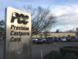 Signage for Precision Castparts Corp. with the company's facility and parking lot visible in the background.