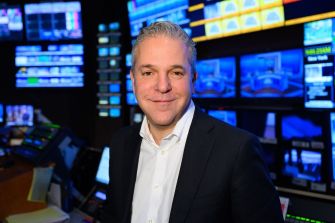 Former ABC producer Michael Corn standing in a broadcast studio filled with screens.