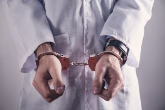 A doctor in handcuffs wearing a white medical coat.