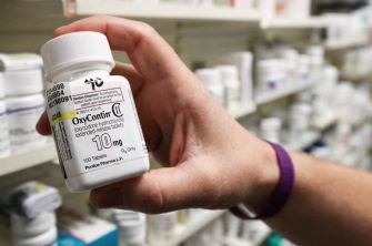 A hand holding a prescription bottle of OxyContin, a powerful opioid medication, with labels visible on the bottle.