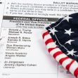 A close-up of a ballot with a black pen and a folded patriotic fabric displaying stars and stripes. A close-up of a ballot with a black pen and a folded patriotic fabric displaying stars and stripes.