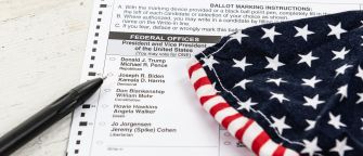 A close-up of a ballot with a black pen and a folded patriotic fabric displaying stars and stripes.