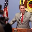 A man speaking at a podium in front of a state seal and American flag. A man speaking at a podium in front of a state seal and American flag.