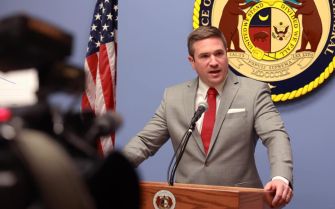 A man speaking at a podium in front of a state seal and American flag.