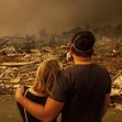 A couple stands together amidst the rubble of destroyed homes, surveying the devastation caused by a wildfire. A couple stands together amidst the rubble of destroyed homes, surveying the devastation caused by a wildfire.