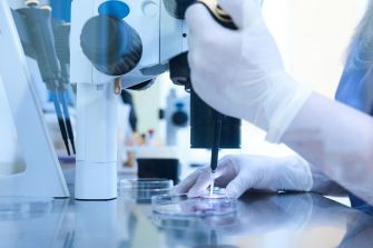 Laboratory technician using a microscope and pipette to work with petri dishes in a fertility clinic setting.