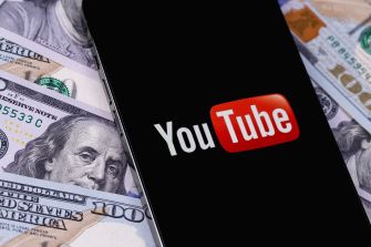 YouTube logo displayed on a smartphone with U.S. dollar bills in the background.