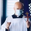 A masked priest holds a wooden cross and a rosary, symbolizing faith during the COVID-19 pandemic. A masked priest holds a wooden cross and a rosary, symbolizing faith during the COVID-19 pandemic.