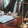 A close-up view of a lawyer's hands writing on legal documents with a scale of justice in the foreground. A close-up view of a lawyer's hands writing on legal documents with a scale of justice in the foreground.