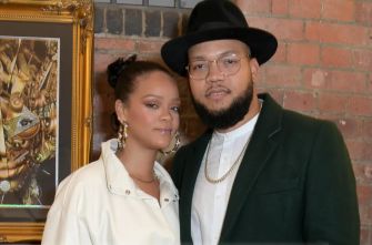 A man and a woman posing together at an event with a brick wall and artwork in the background.