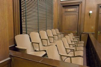 A row of jury seats in a courtroom, showing wooden walls and blinds.