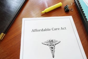 Document titled "Affordable Care Act" with a medical symbol on top of a wooden desk, accompanied by a highlighter and a binder clip.