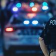 Police officer standing near a police car with flashing lights in a public setting. Police officer standing near a police car with flashing lights in a public setting.