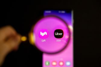 Logos of Lyft and Uber displayed on a smartphone screen, with a magnifying glass focusing on them.