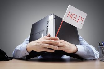A person hiding behind a laptop, holding a sign that says "HELP!"
