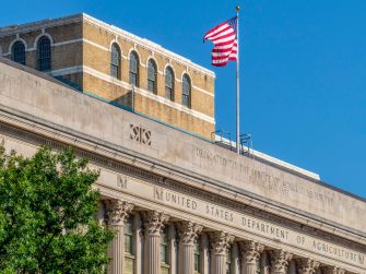 The facade of the United States Department of Agriculture building with an American flag waving above.