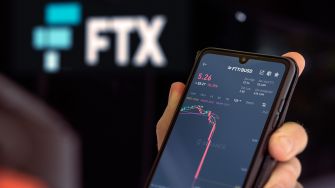 A person holding a smartphone displaying cryptocurrency market data, with the FTX logo in the background.