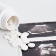 Pills scattered on a surface next to ultrasound images and an overturned prescription bottle. Pills scattered on a surface next to ultrasound images and an overturned prescription bottle.
