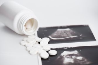 Pills scattered on a surface next to ultrasound images and an overturned prescription bottle.