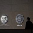 A person walking past the logos of the Office of the Comptroller of the Currency (OCC) and the Federal Housing Finance Agency (FHFA) on a wall. A person walking past the logos of the Office of the Comptroller of the Currency (OCC) and the Federal Housing Finance Agency (FHFA) on a wall.